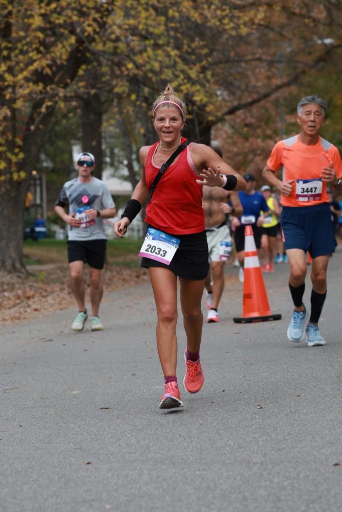 Woman running in race, smiling, waving at camera